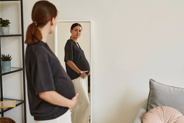 Těhotná žena dívá na břicho v zrcadle — Stock fotografie