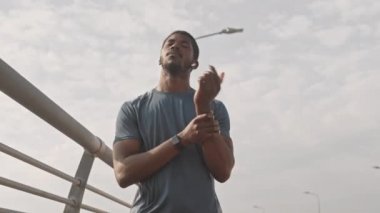 Düşük açılı orta yaşlı, kablosuz kulaklıklı genç Afro-Amerikan sporcu sabah koşudan önce dışarıda ısınıyor.