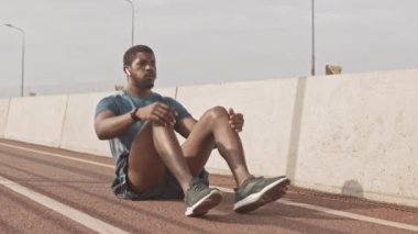 Afrika kökenli Amerikalı sporcu ya da spor kıyafetleri ve kablosuz kulaklıklarla güneşli bir sabahta koşu pistinde mekik çekerken çekilmiş yavaş çekim.