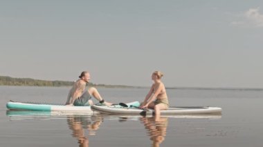 Güneşli bir günde gölde yemek masasında oturmuş sohbet eden ve yaz tatilinin tadını çıkaran genç bir çiftin yavaş yavaş geniş açılışı.