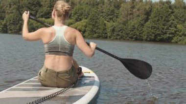 Gölde kürek çeken, yemek masasında oturan, yavaş, genç, beyaz bir kadının dikiz görüntüsü.