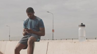 Spor kıyafetli bir Afro-Amerikalının sabah antrenmanından sonra açık havada telefon konuşması yaparken yavaş çekimde.