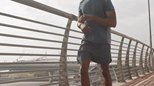 ミッドセクションスローモショットのフィットアフリカ系アメリカ人男性アスリートは 彼のスマートウォッチでタイマーを見て 晴れた朝にレーストラックに沿ってジョギング — ストック動画