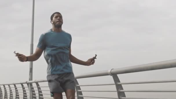 晴天户外运动时 穿着运动服和无线耳机跳绳的非洲裔美国男子中慢镜头 — 图库视频影像