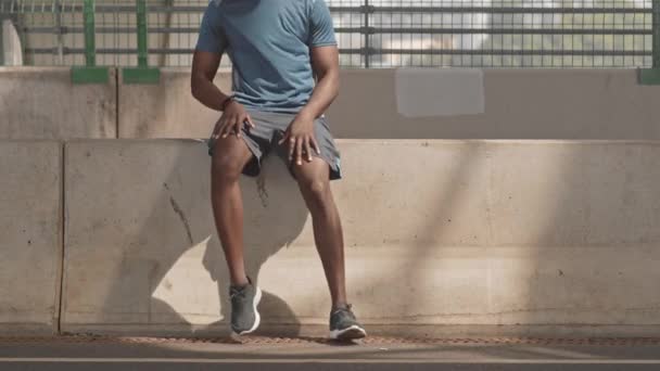 都市環境でスポーツウェアジョギングで認識できないフィットアフリカ系アメリカ人の男の作物のショットは 息を取るために座って — ストック動画