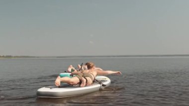 Genç, aktif bir çiftin yemek masasında karnının üstünde yatarken gölde kürek çekerken, sonra da yemek sörfü yapmak için ayakta duran bir kadının dikiz görüntüsü.
