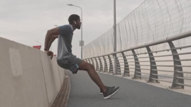Kentteki köprü duvarına karşı ters şınav çeken atletik Afro-Amerikalı adamın yavaş çekimi.