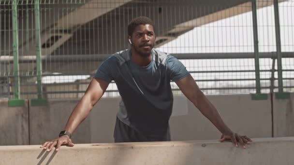 街の橋で壁を押しのけて朝一人で訓練するアフリカ系アメリカ人の強い男のスローショット — ストック動画