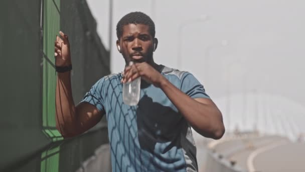 穿着运动服的非洲裔美国男子在室外慢跑时 站在阳光下喝水 呼吸和休息的中速镜头 — 图库视频影像