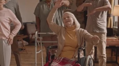 Huzurevinde hemşireden sonra tekrar eden fiziksel egzersiz yapan bir grup aktif çok ırklı yaşlının yavaş çekimi.
