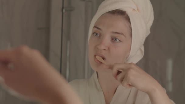年轻迷人的刷牙女子穿着浴衣 头戴毛巾 照镜子 中等程度地近距离观察自己 — 图库视频影像