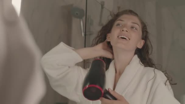 在大理石浴室的镜子前 穿着白色浴衣的快乐的年轻白人妇女正在擦干她长长的卷曲的头发 这是她的中等特写镜头 — 图库视频影像