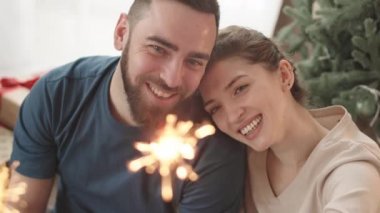 Güzel mavi gözlü beyaz bir çiftin yüksek açılı göğüsleri evde durmuş gülümsüyor ve parlayan Bengal ışığına bakıyor, kadın erkeği öpüyor.