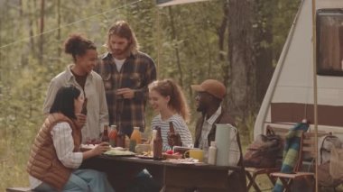 Çok ırklı beş yetişkinin ormanda öğle yemeği yerken, yazın tekerlekli sandalyede birlikte otururken ağır çekimde.