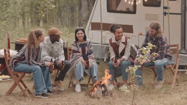 5名年轻的多族裔男子和妇女坐在森林篝火边喝啤酒和谈话时的慢镜头 — 图库视频影像