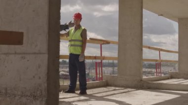 Güneşli bir günde, inşaat halindeki binanın içinde kask takan iki beyaz erkek inşaat işçisinin izini sürüyorum.