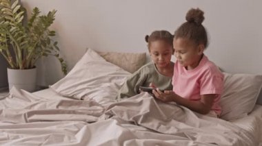 5 yaşında, Afro-Amerikan iki tatlı kızın akıllı telefondan oyun oynamalarının ve evlerinde rahat bir şekilde oturmalarının yavaş çekimi.