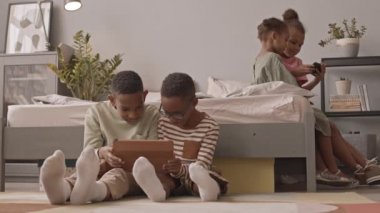 Dört Afro-Amerikan okul öğrencisinin rahat evlerinde otururken, kızların akıllı telefondan oyun oynarken, erkeklerin dijital tablette komik videolar izlediği yavaş çekim.