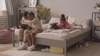 Konforlu evde boş vakitlerinde alet kullanan dört Afro-Amerikan öğrencinin yavaş çekimleri. Kızlar akıllı telefondan komik videolar izlerken erkekler dijital tablette oyun oynuyor