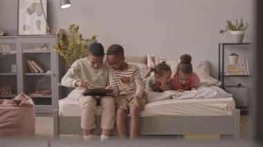 Bir grup Afro-Amerikalı öğrencinin boş zamanlarını hoş bir dairede aletlerle geçirmesinin yavaş çekimi. Dijital tablette oyun oynayan oğlanlar ve akıllı telefondan video izleyen kızlar