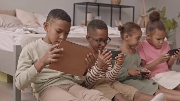 4人のアフリカ系アメリカ人の学校の男の子と女の子のスローモ中のショットは デジタルタブレットやスマートフォンで仮想ゲームをプレイガジェットに中毒 — ストック動画