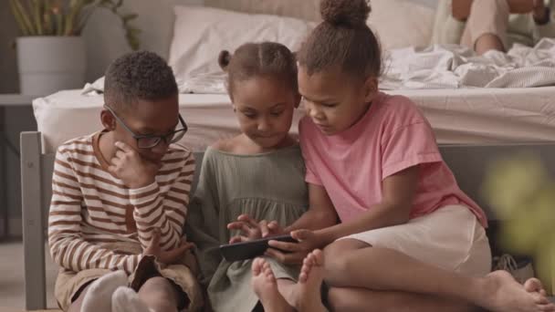 アフリカ系アメリカ人の子供たちの遅いショット床の上に座っていますベッドの近くにビデオを見ますスマートフォン — ストック動画