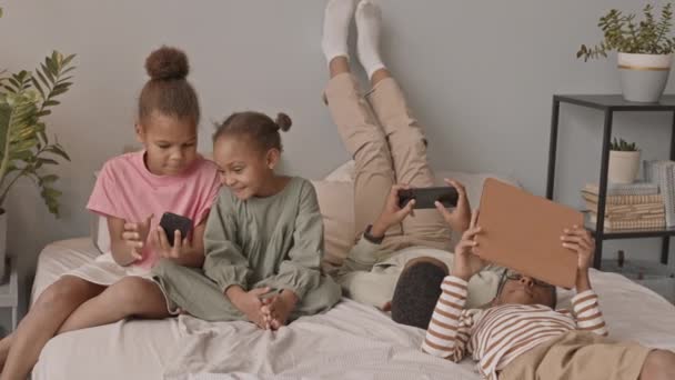 在舒适的现代公寓里 一群快乐的非洲裔美国男生和女生坐在床上玩着不同的小玩艺儿 慢镜头闪烁着 — 图库视频影像
