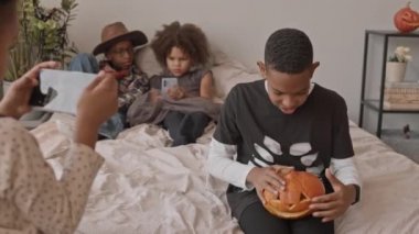 12 yaşındaki Afro-Amerikan çocuğun şeker için balkabağı kovası tutarken çekilmiş yavaş çekimleri. Cadılar Bayramı partisinde arkadaşının elinde tuttuğu akıllı telefondan konuşuyor.