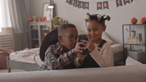スローモショットの可愛いです5歳のアフリカ系アメリカ人の女の子と彼女の兄を持っています楽しいビデオを見たり ハロウィンパーティー中にスマートフォンでゲームをプレイ — ストック動画