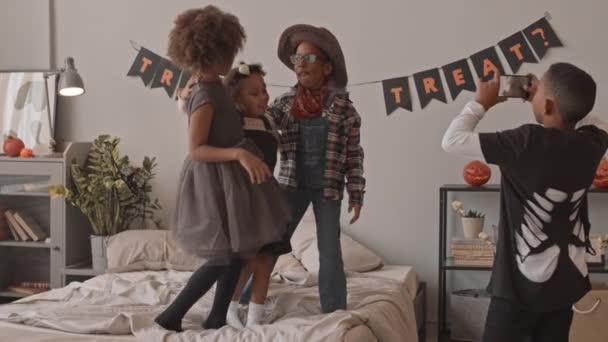 Slowmo záběr hravé afroamerické školáky v halloweenských kostýmech natáčení legrační strašidelné videa na smartphone během domácí halloween party