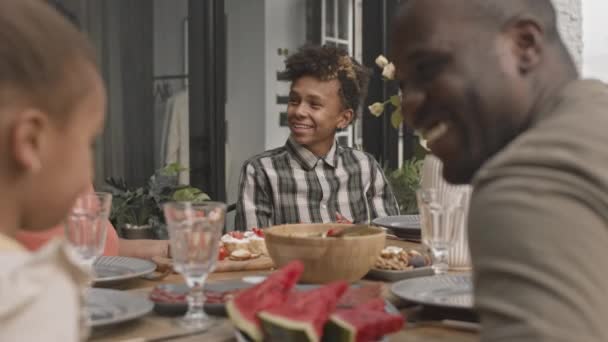 Średnie Zbliżenie Nastoletniego Afrykańskiego Chłopca Uśmiechniętego Rozmawiającego Członkami Rodziny Siedzącymi — Wideo stockowe