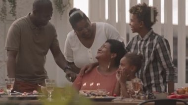 Orta uzunlukta Afrikalı bir çocuk, olgun bir kadının arkasında duruyor torunuyla masada oturuyor, doğum günü pastasının üzerindeki mumları üflüyor.