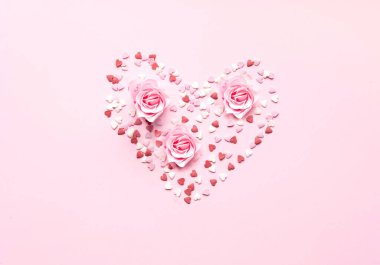 Sevgililer Günü. Pembe arka planda gül çiçeğiyle tatlı konfetiden oluşan kalp şekli. Tebrik kartı ya da metin tasarımının şablonu. Yakın çekim, yaratıcı kopya alanı