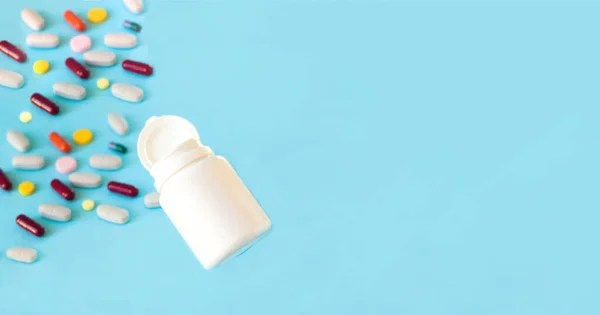 Capsules spilling out of white bottle. Multicolored medical pills on a blue background. Treatment of coronavirus symptoms, medicine concept. — Fotografia de Stock