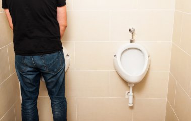 Adam banyoda beyaz bir pissoir önünde duran