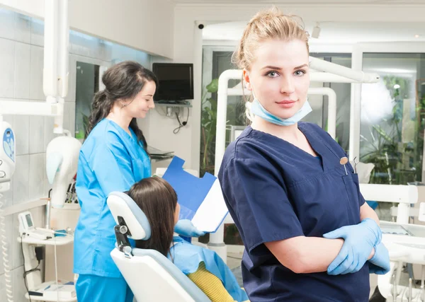 Kvinnlig assistent med patienten i backgound och tandläkare framför — Stockfoto