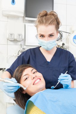 Gülümseyen hasta ve diş hekimi üniforma ve maske giyiyor