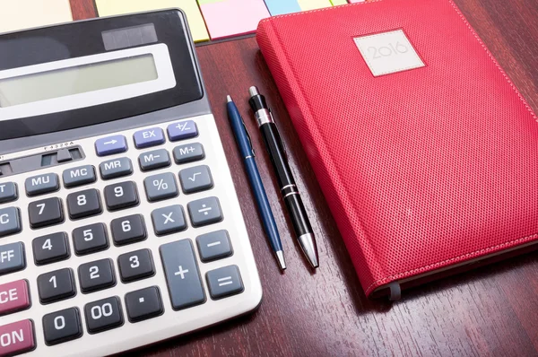 Wooden desktop with red agenda and calculator — 스톡 사진