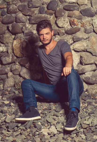 Junger Mann in Jeans und grauem T-Shirt setzt sich — Stockfoto