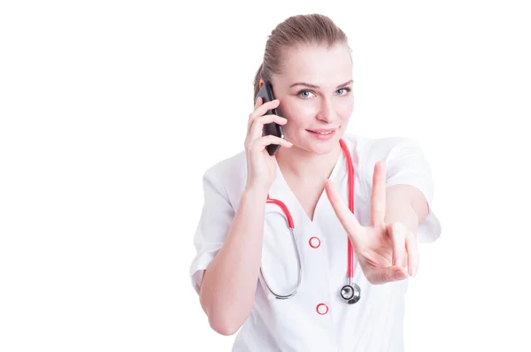 Beautiful female doctor holding phone and showing peace gesture — Stock Photo, Image