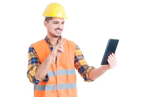 Construtor sorridente usando tablet e mostrando paz ou vitória ge — Fotografia de Stock