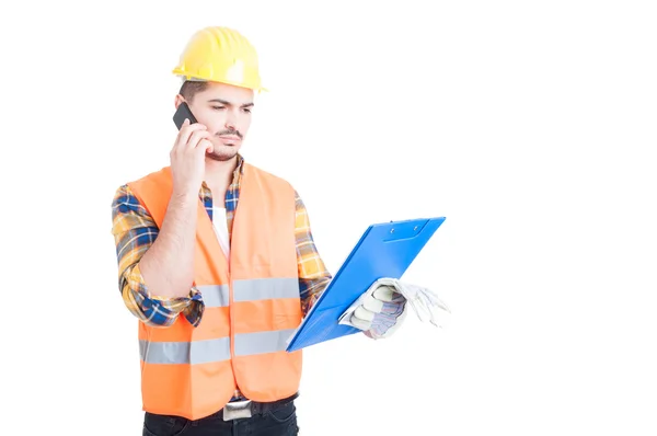 Joven constructor sosteniendo un portapapeles mientras habla en smartphon —  Fotos de Stock
