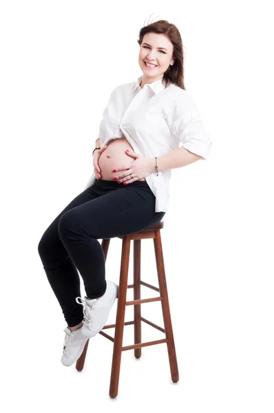 Vackra gravid sitter på stol och hålla händerna på magen — Stockfoto