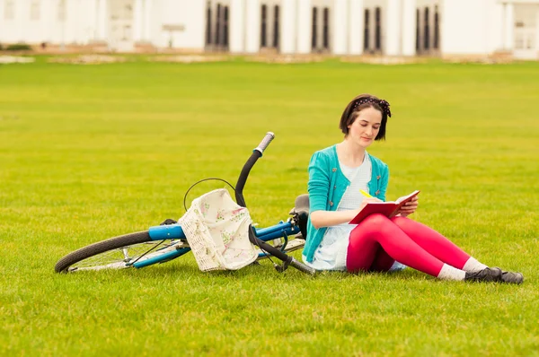 Giovane hipster femmina con bicicletta scrivere qualcosa su notebook — Foto Stock