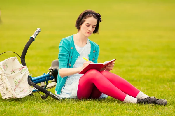 Donna attraente siede su erba verde e scrivere su notebook — Foto Stock