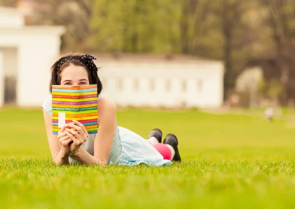 Carino e divertente giovane femmina si nasconde dietro il libro — Foto Stock