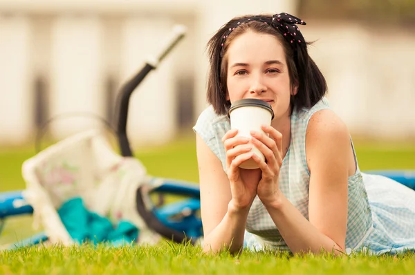 Mulher feliz com xícara de café deitado na grama — Fotografia de Stock