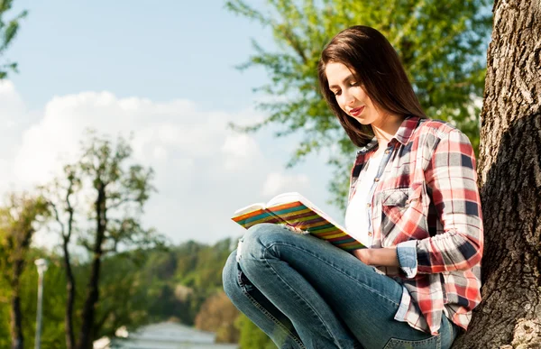 Mujer leyendo junto a un árbol en el parque — Foto de Stock