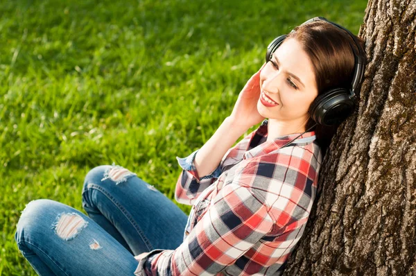 Genç kadın parkta ağaç altında rahatlatıcı gülümseyen — Stok fotoğraf