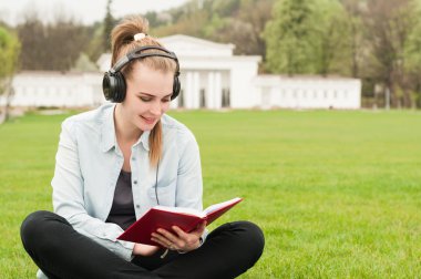 Güzel gülümseyen kadın müzik zevk ve parkta okuma